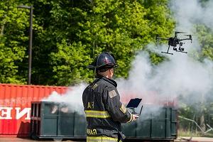 Firefighter in uniform flying drone with smoke in background